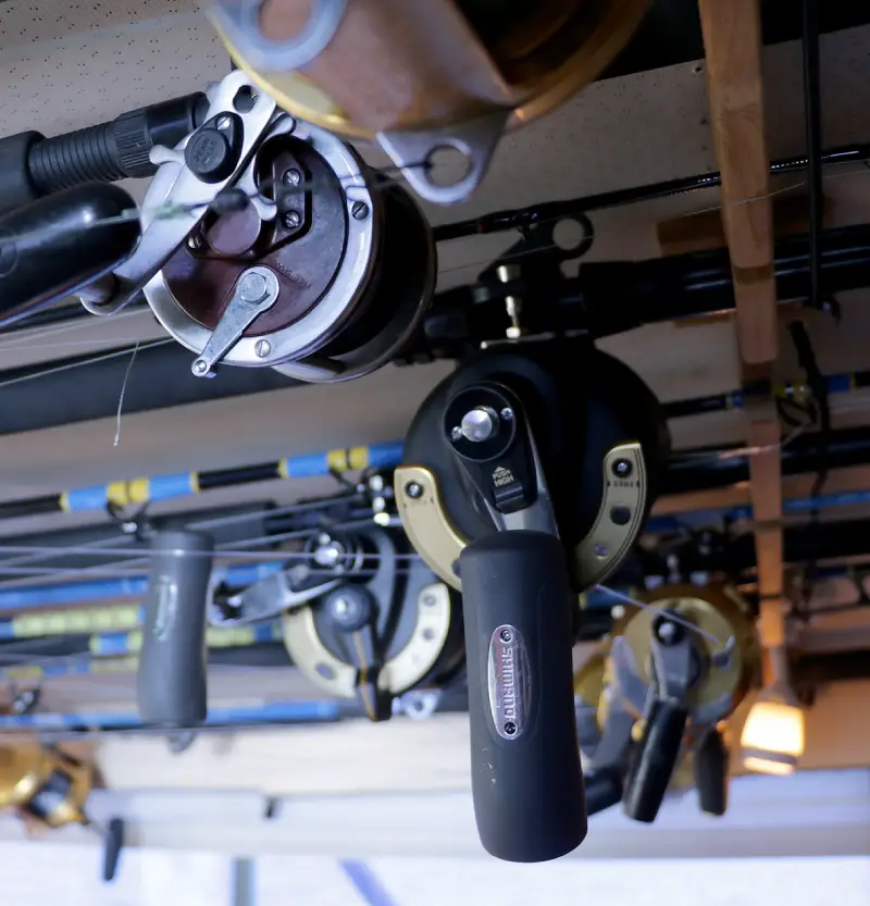 New - os1 A collection of fishing rods and reels hanging from a ceiling, showcasing various fishing gear in an organized display.