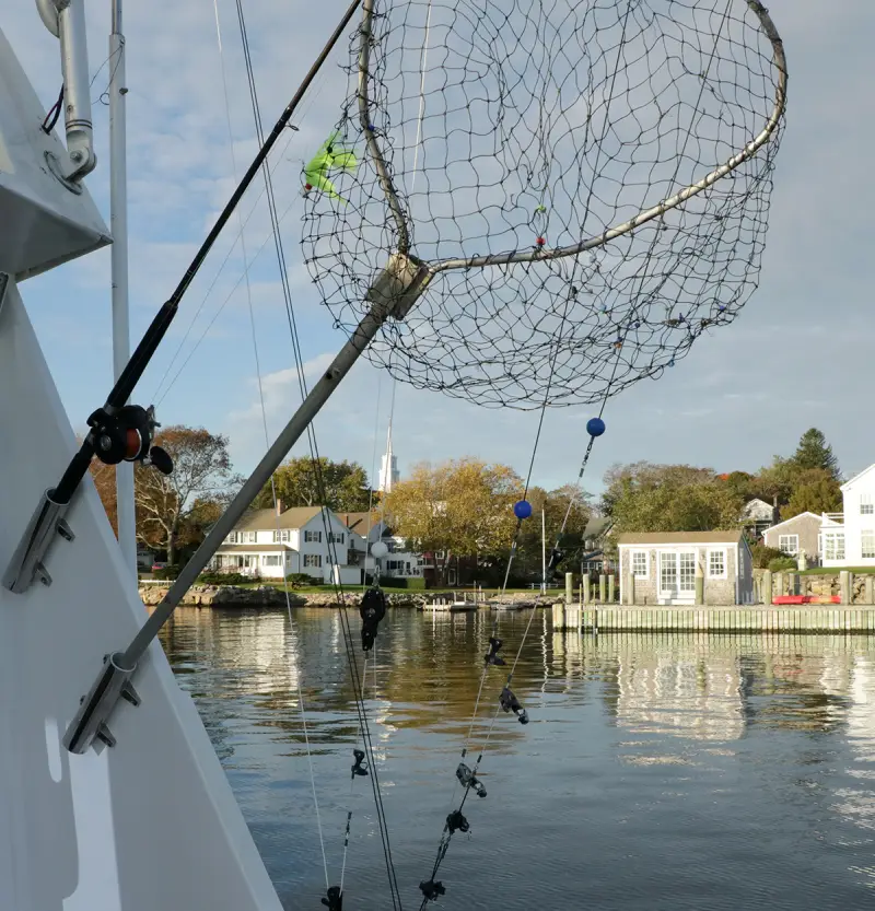 new os2 A fishing net attached to a boat, with colorful buoys, overlooking calm waters and picturesque houses along the shoreline.