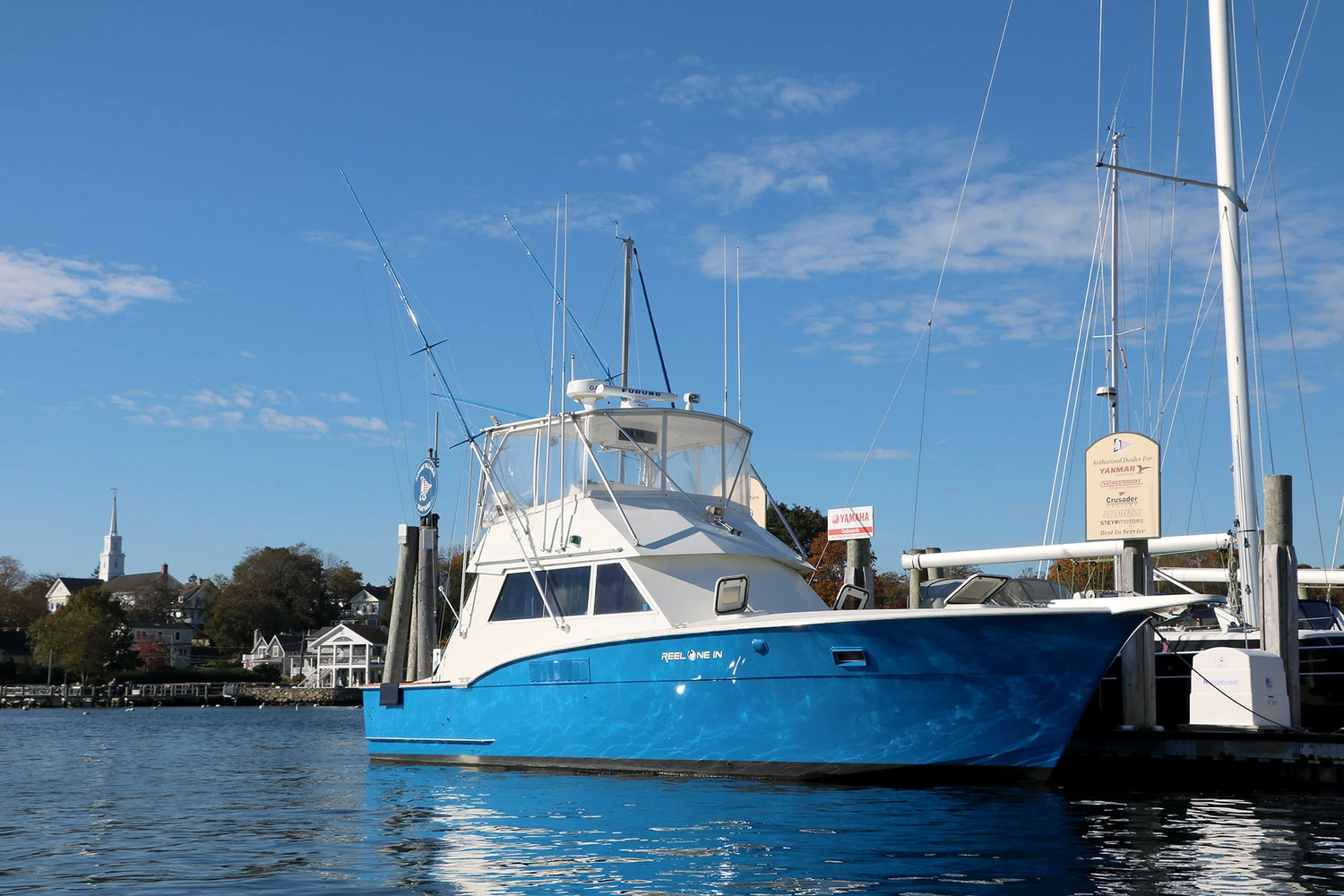 sub banner 1 A blue fishing boat named "Reel One In" docked at a marina under a clear blue sky, with buildings and a church steeple in the background.